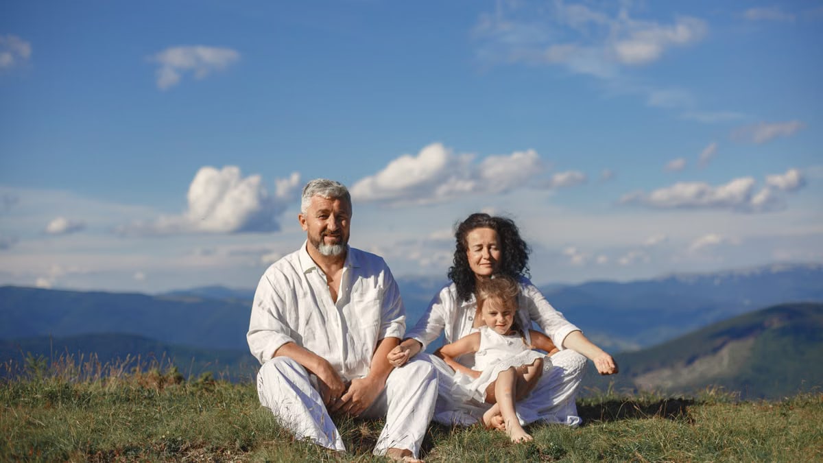 A happy family enjoys a sunny day outdoors, sitting together on a grass field.