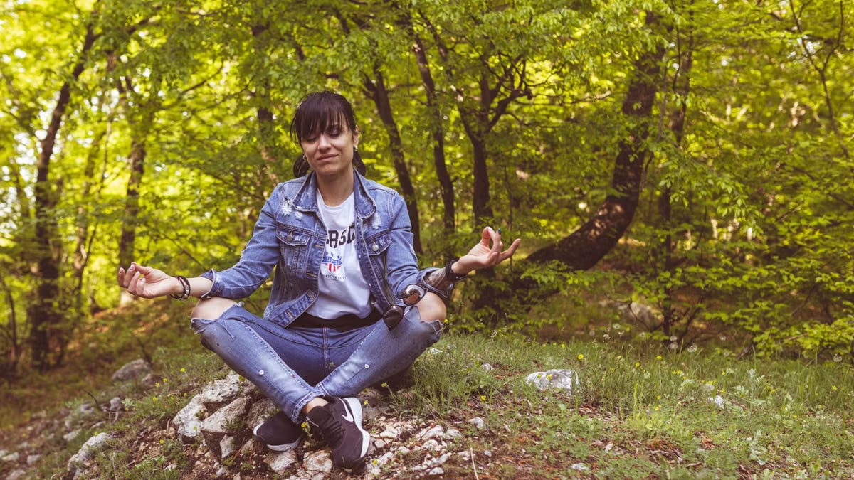 A woman meditates peacefully in a lush green forest, exuding calm and relaxation.